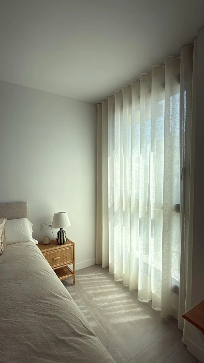 Dormitorio luminoso con visillo blanco translúcido junto a la cama